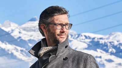 Ein Mann mit Brille steht vor einem Bergpanorama.